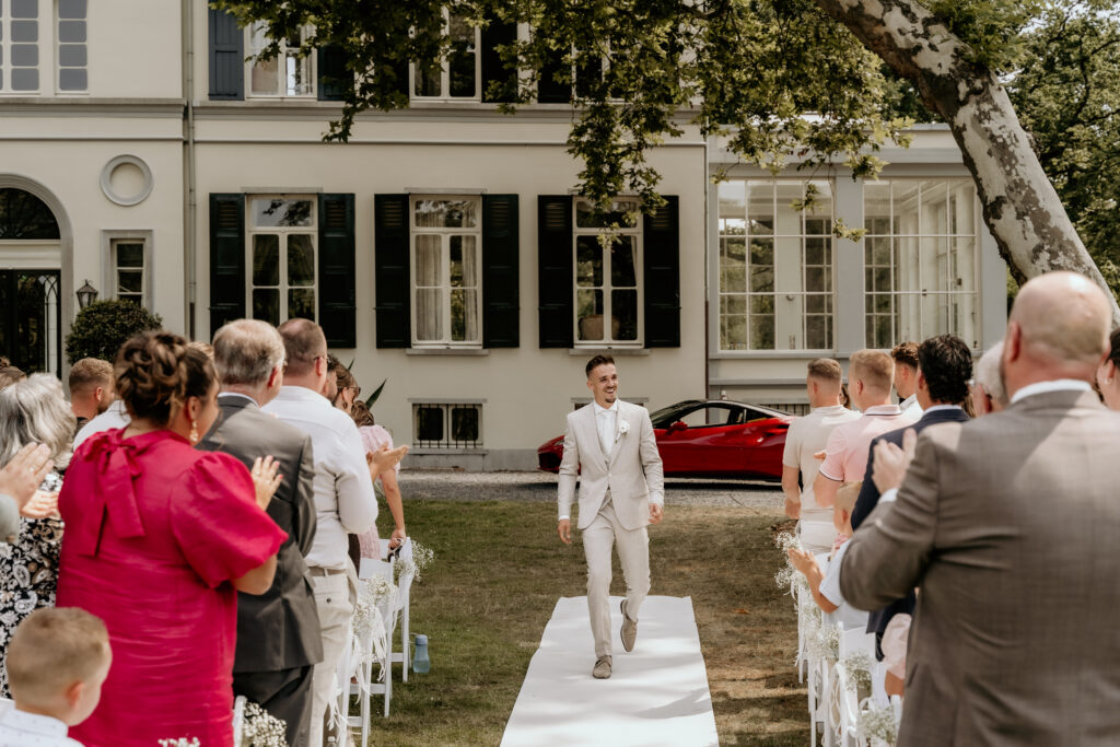 Bruidegom loopt naar ceremonie van buitenbruiloft bij Landgoed Mattemburgh